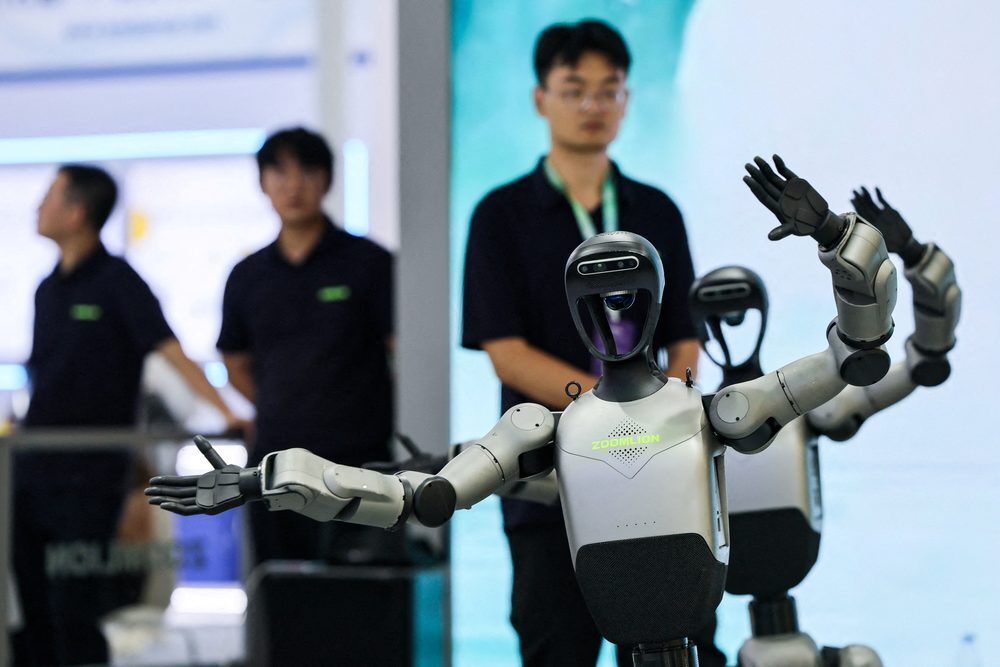 Humanoid robot with raised arms at a technology exhibition, with engineers in the background observing a demonstration
