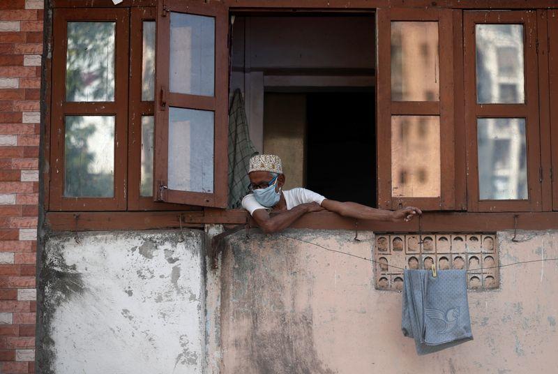 A man wearing a protective face mask looks out of the window during a 21-day nationwide lockdown to limit the spreading of coronavirus disease (COVID-19) in Mumbai, India, April 4, 2020. REUTERS/Francis Mascarenhas - RC2PXF97FKQX