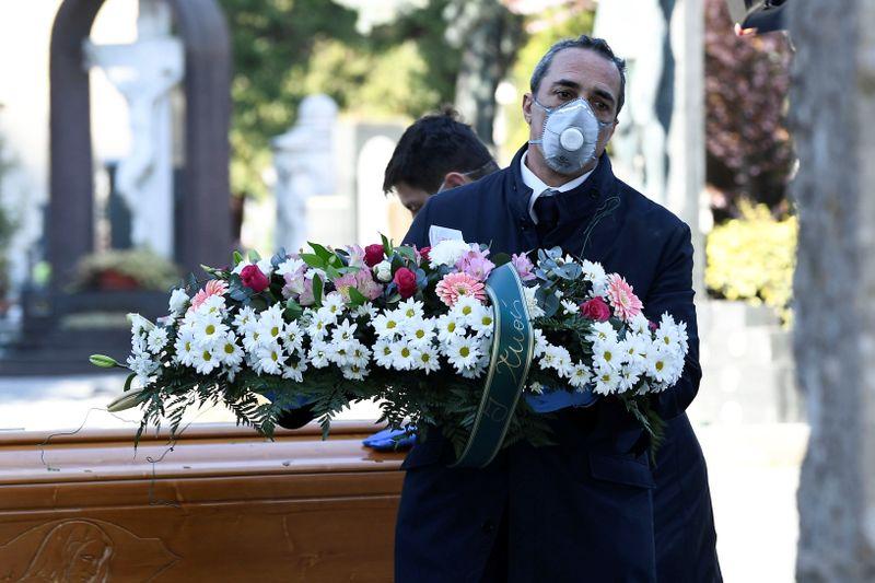 Cemetery workers and funeral agency workers in protective masks transport a coffin of a person who died from coronavirus disease (COVID-19), into a cemetery in Bergamo, Italy March 16, 2020. REUTERS/Flavio Lo Scalzo
