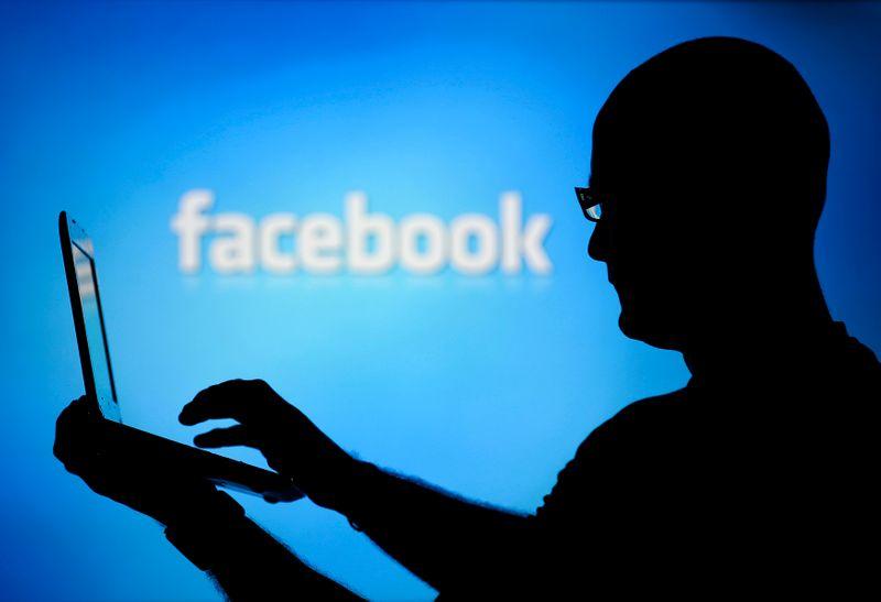 A man is silhouetted against a video screen with an Facebook logo as he poses with an Dell laptop in this photo illustration taken in the central Bosnian town of Zenica