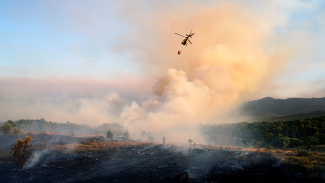 A firefighting helicopter makes a water drop as a wildfire burning in the village of Navalmoral