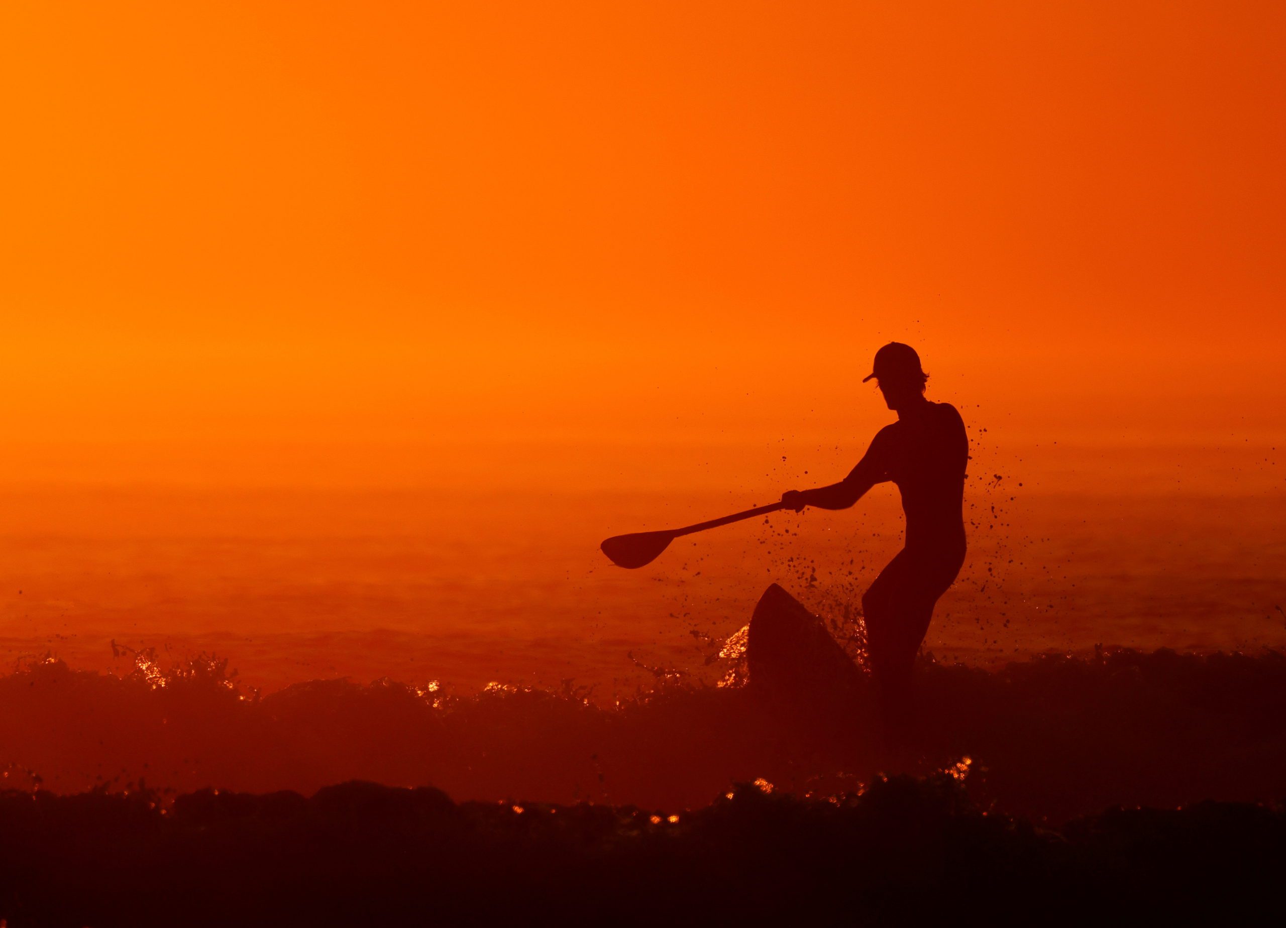 A man on a paddle board surfs as a heat wave hits France