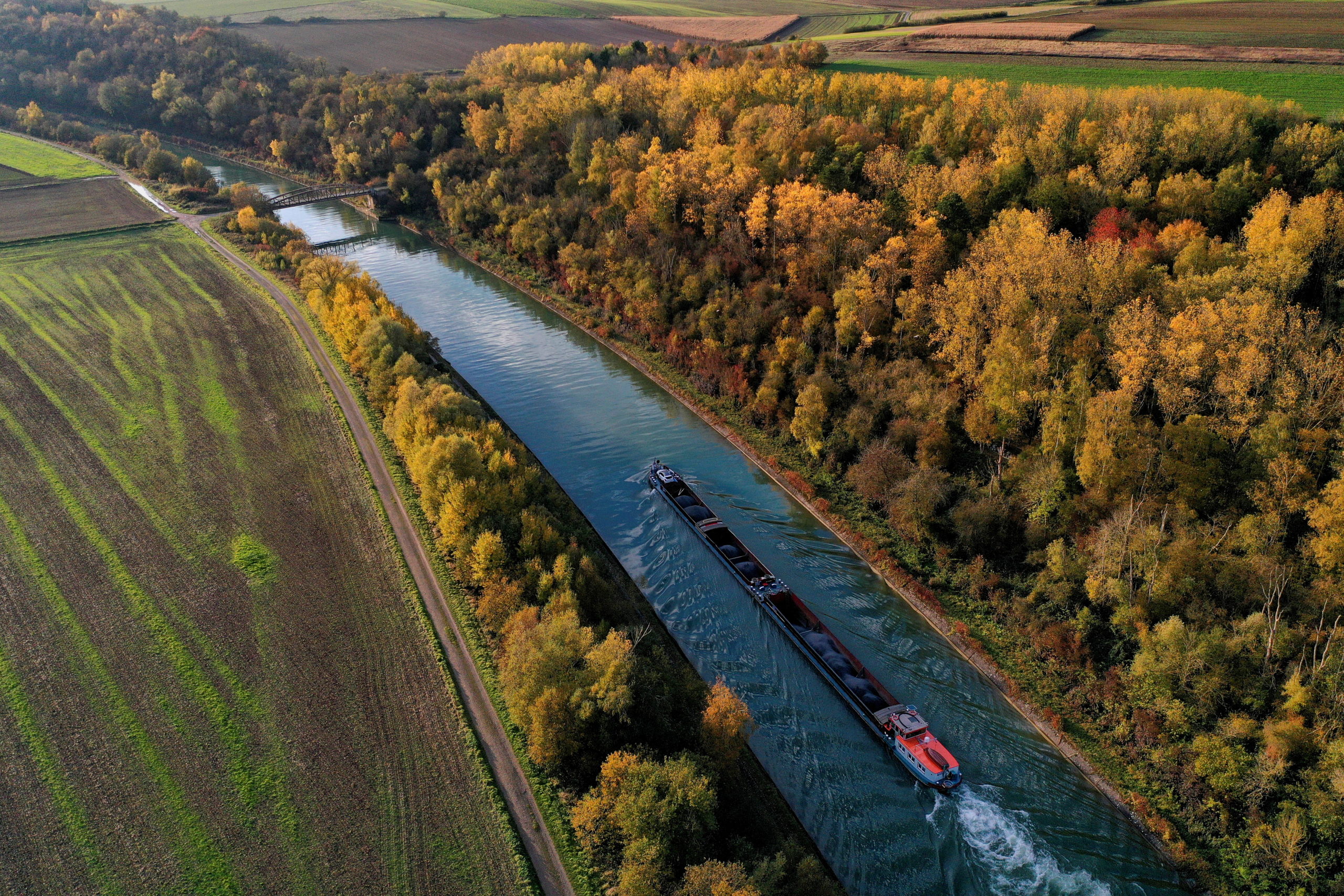 Golden and rusty leaves colour the autumn as a river barge navigates on the Canal du Nord in Ruyaulcourt