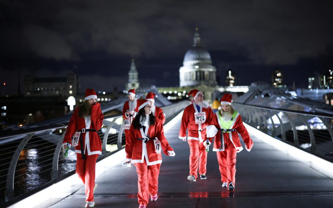 People dressed as Santa Claus walk over Millennium Bridge before taking part in a fun run on the South Bank in London