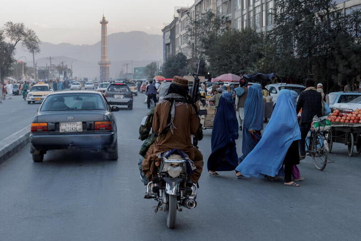 FILE PHOTO: A group of women wearing burqas crosses the street as members of the Taliban drive past in Kabul, Afghanistan October 9, 2021. REUTERS/Jorge Silva/File Photo