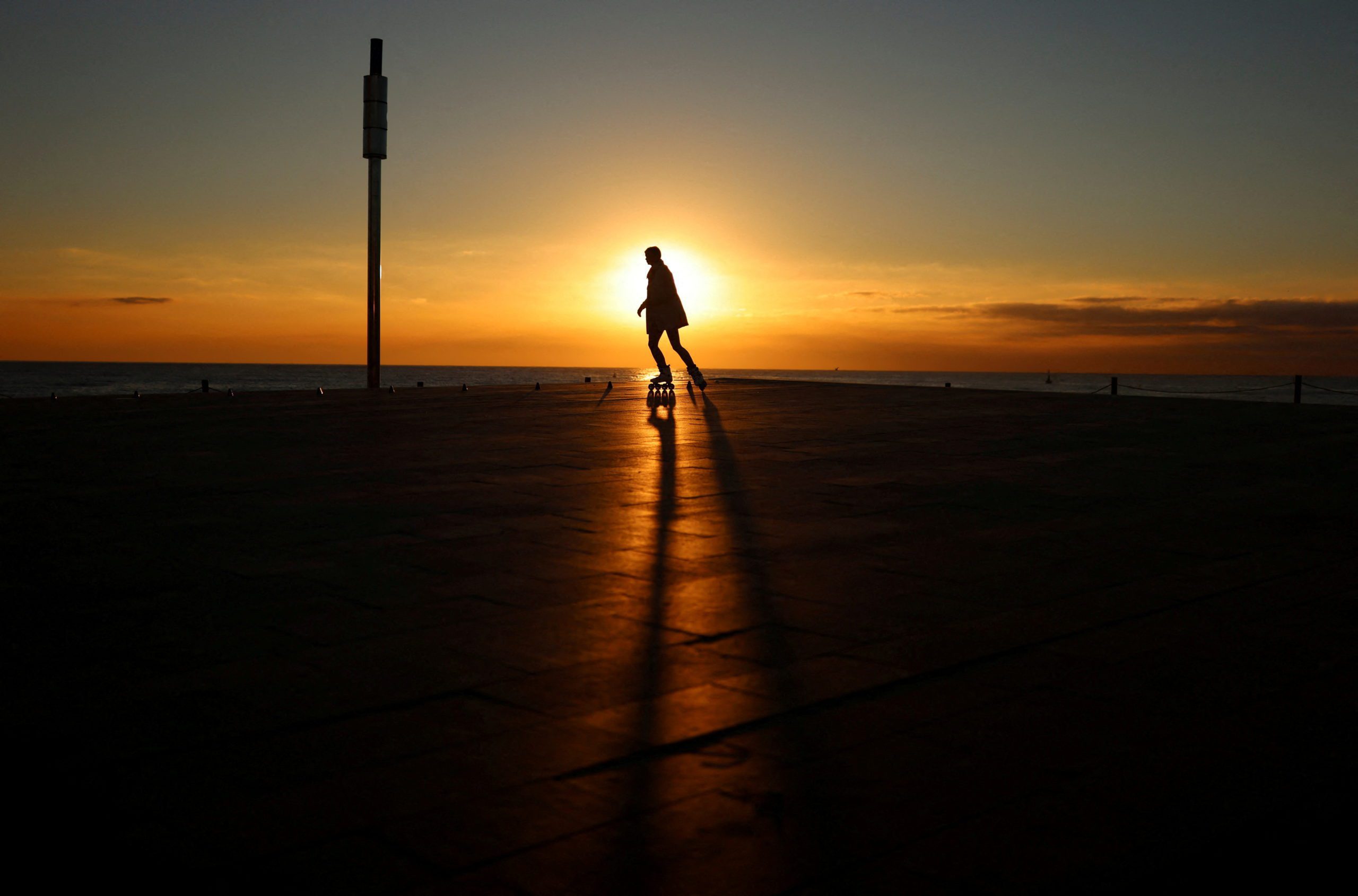 A woman skates during sunrise at the sidewalk of Barceloneta beach in Barcelona